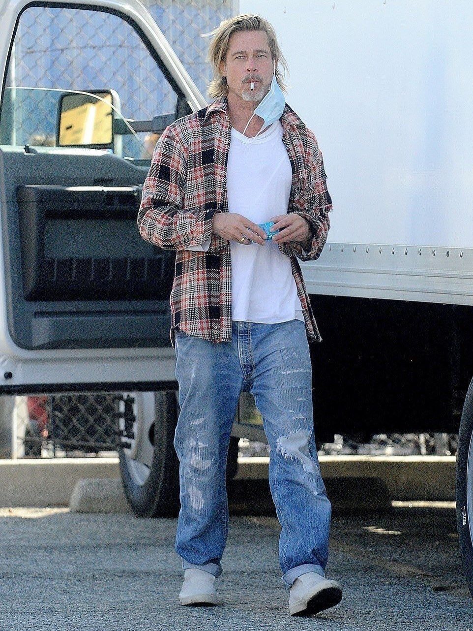 Man walking in a red and black plaid flannel shirt and ripped blue jeans.