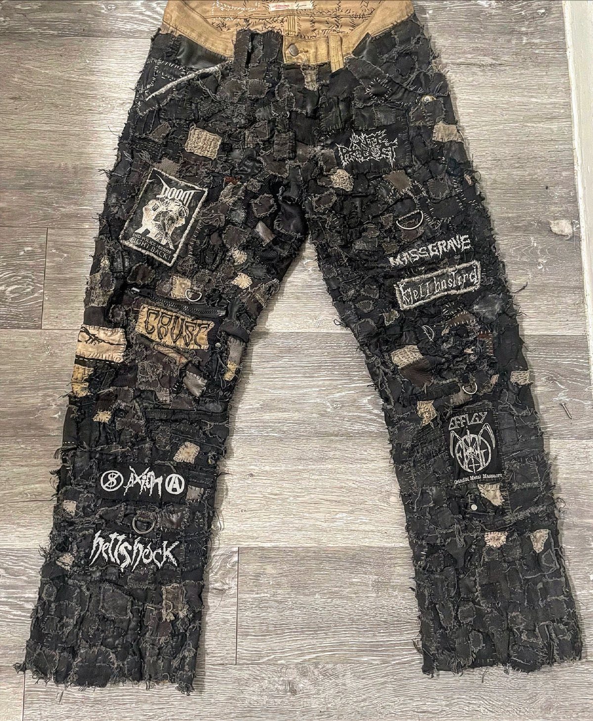 Black distressed denim pants covered in various fabric patches and white graphic prints.