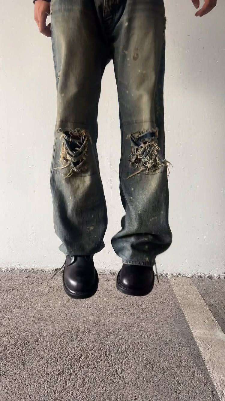Distressed grey denim jeans with large frayed rips at the knees and black boots.