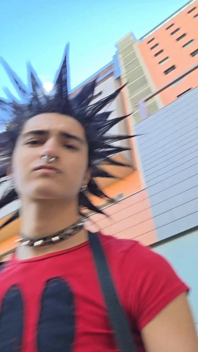A person with black spiked hair, a nose ring, and a spiked collar wearing a red t-shirt.