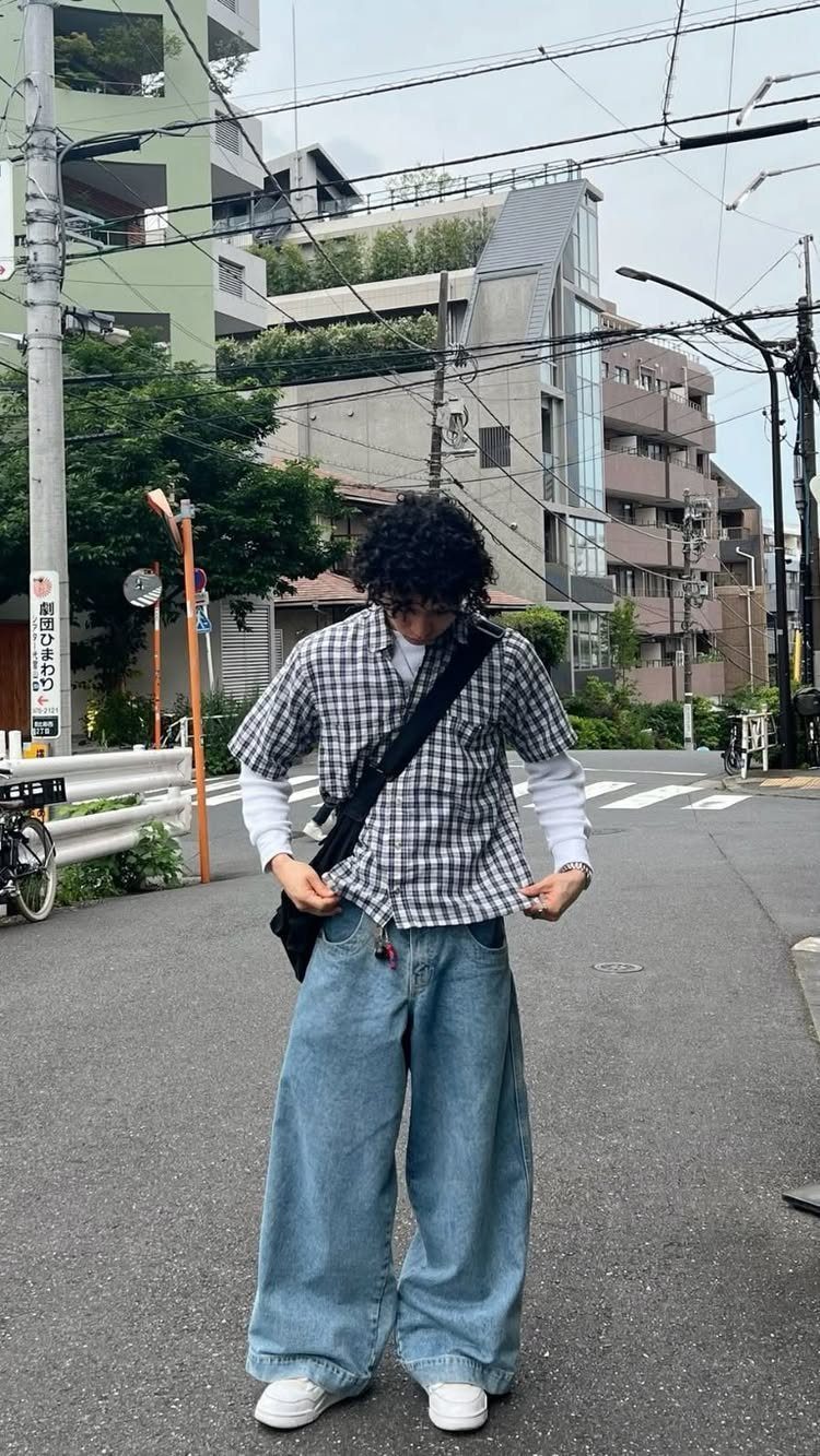 A person wearing a checkered shirt and extremely wide-leg blue denim baggy pants on a city street.