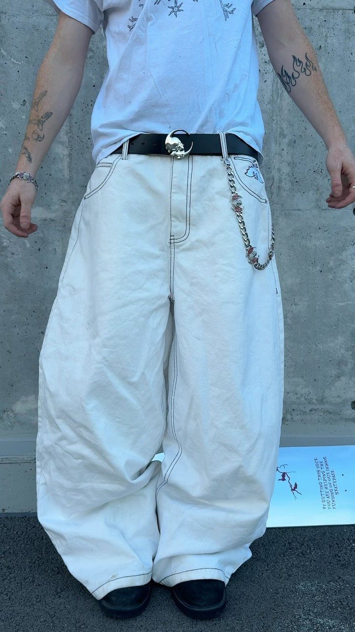 Person wearing extremely baggy white wide-leg trousers with dark contrast stitching and a silver chain belt.