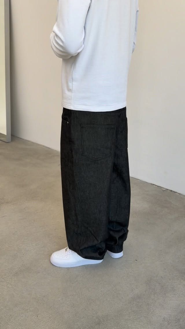 Person wearing a white long-sleeved shirt, oversized black baggy trousers, and white sneakers.
