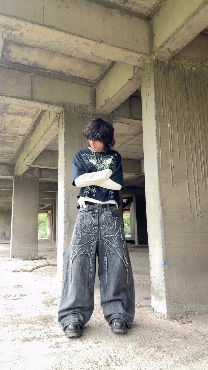 A person wearing oversized dark denim pants and a graphic t-shirt standing in a concrete building.