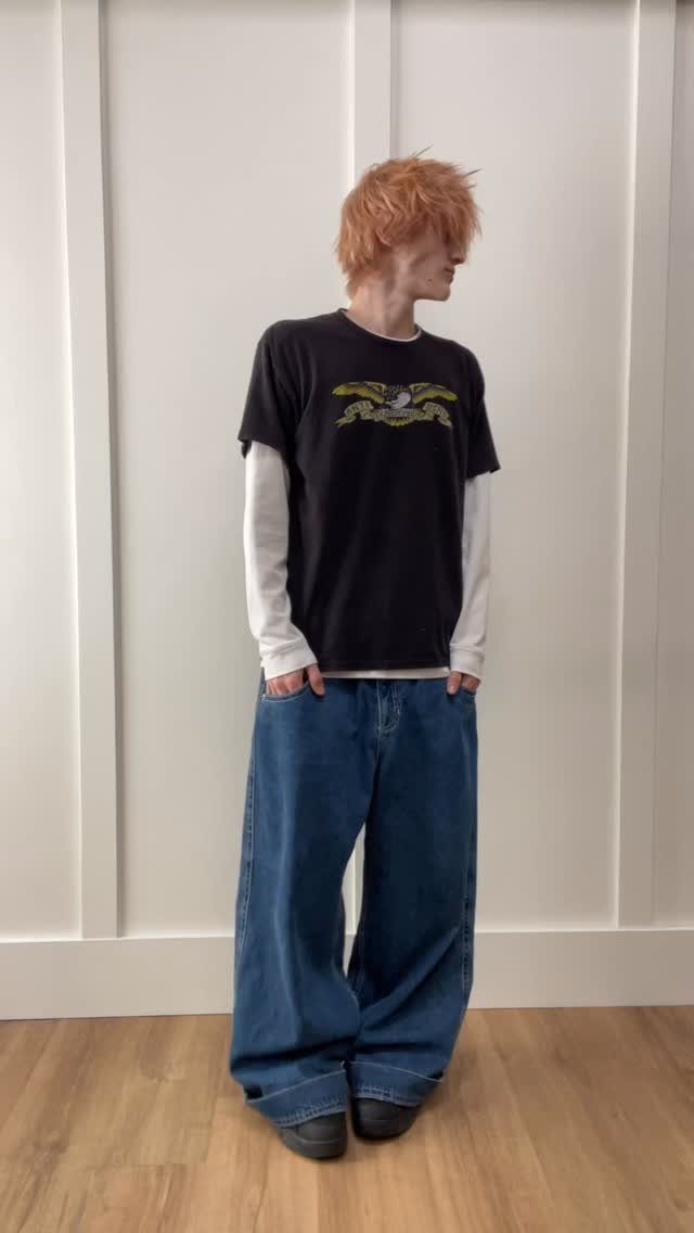 Person with orange hair wearing a black graphic tee and baggy blue denim pants.