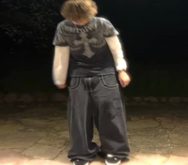 A person wearing a dark graphic t-shirt with a large white cross and baggy pants.