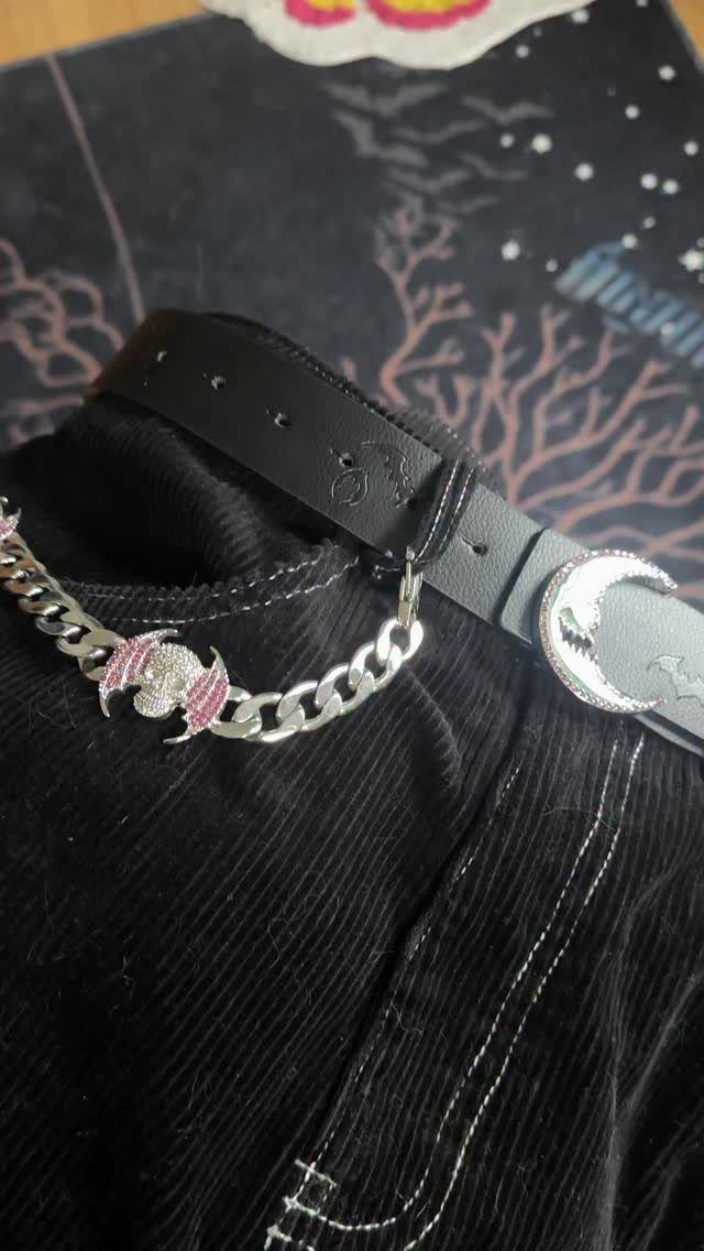 Black leather belt with a silver moon buckle and pink bat chain on black corduroy pants.