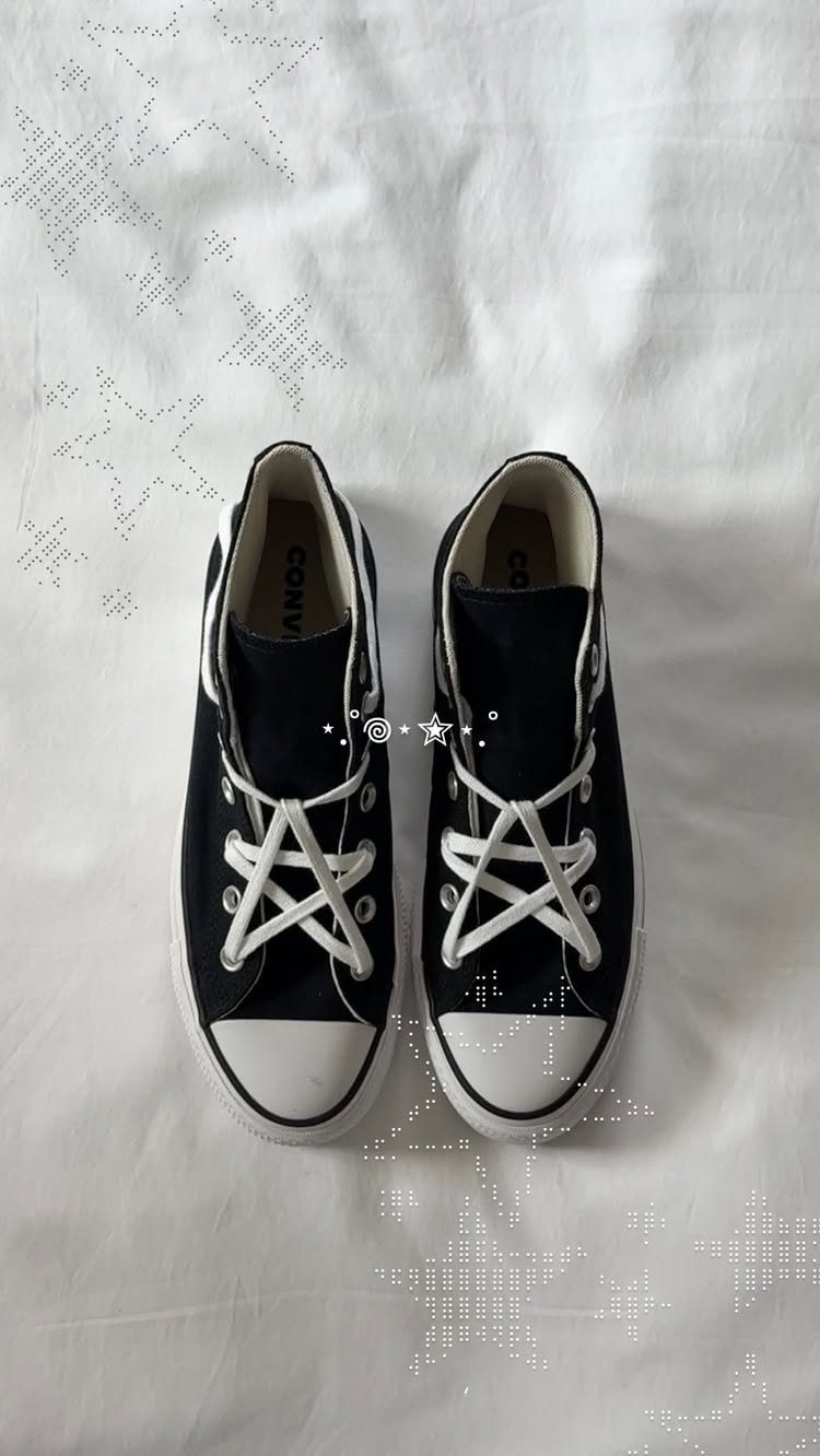 Black high-top Converse sneakers with white laces resting on a white textured fabric background.