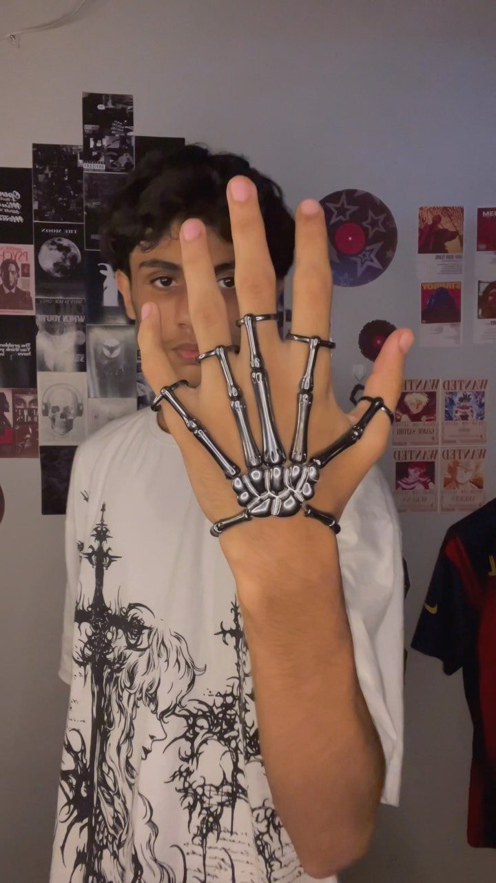 Young man wearing a silver skeleton hand ring and a graphic t-shirt against a poster-covered wall.