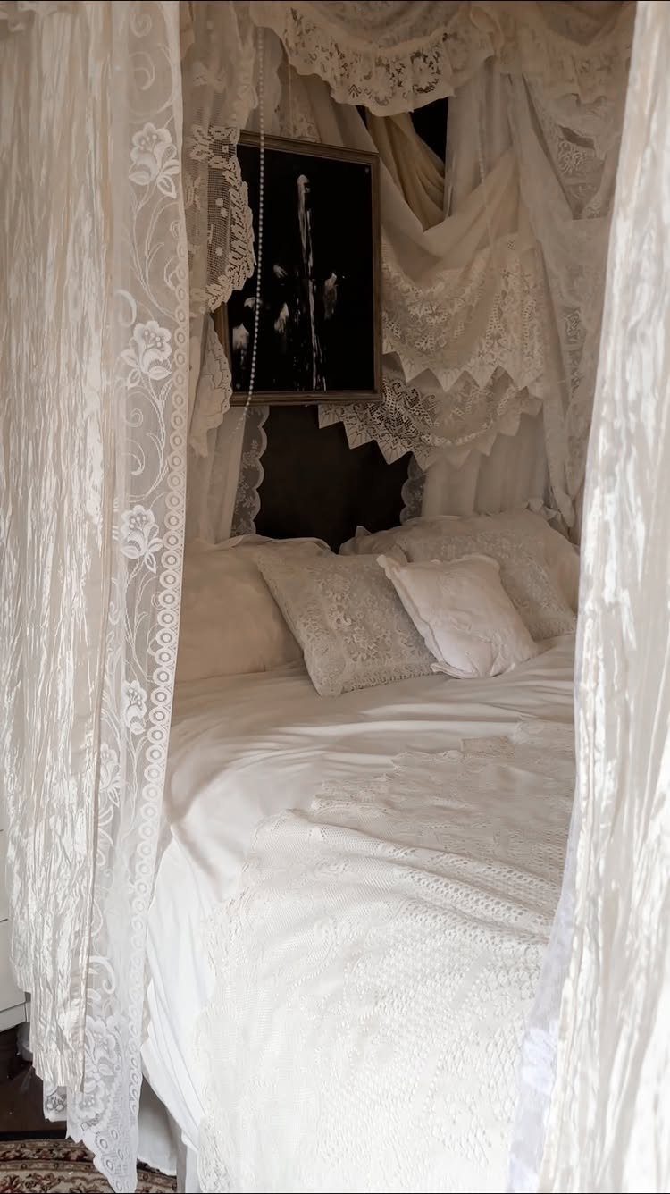 White lace bedding and canopy curtains surrounding a bed with a dark framed picture on the wall.