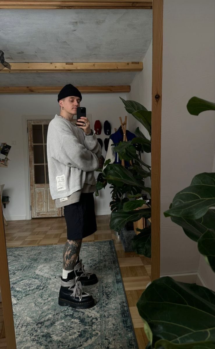 A person wearing black combat boots and a grey sweatshirt posing for a mirror selfie.