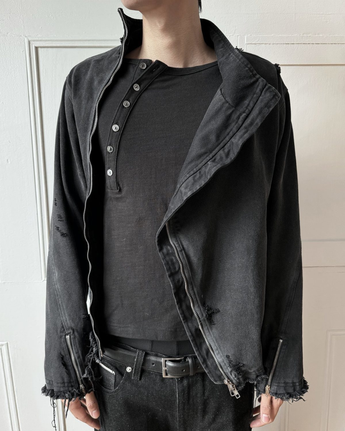 A person wearing a black textured denim jacket over a black henley shirt and dark jeans.