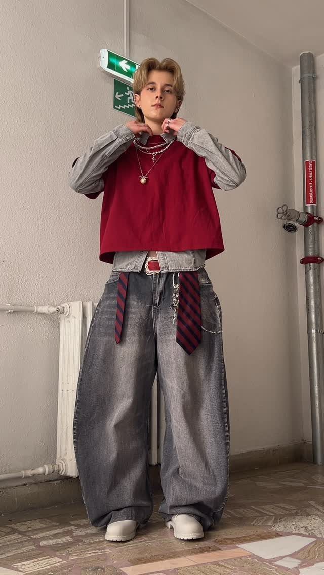 A person wearing a red cropped shirt and oversized wide-leg denim jeans in a hallway.