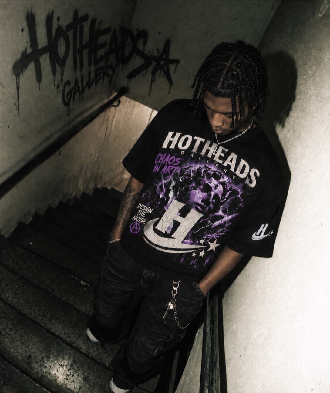 A young man in a black graphic t-shirt posing in a dark stairwell.