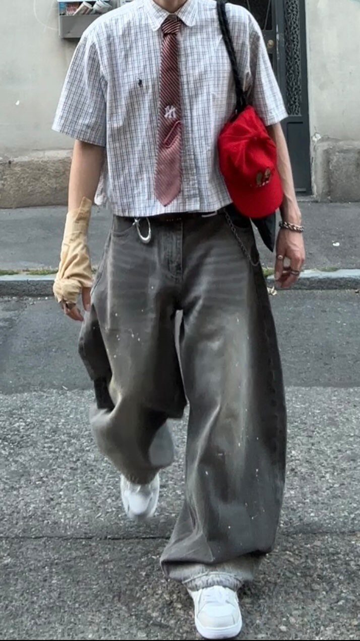 A person walking down a street wearing oversized checkered clothing, a tie, and baggy trousers.