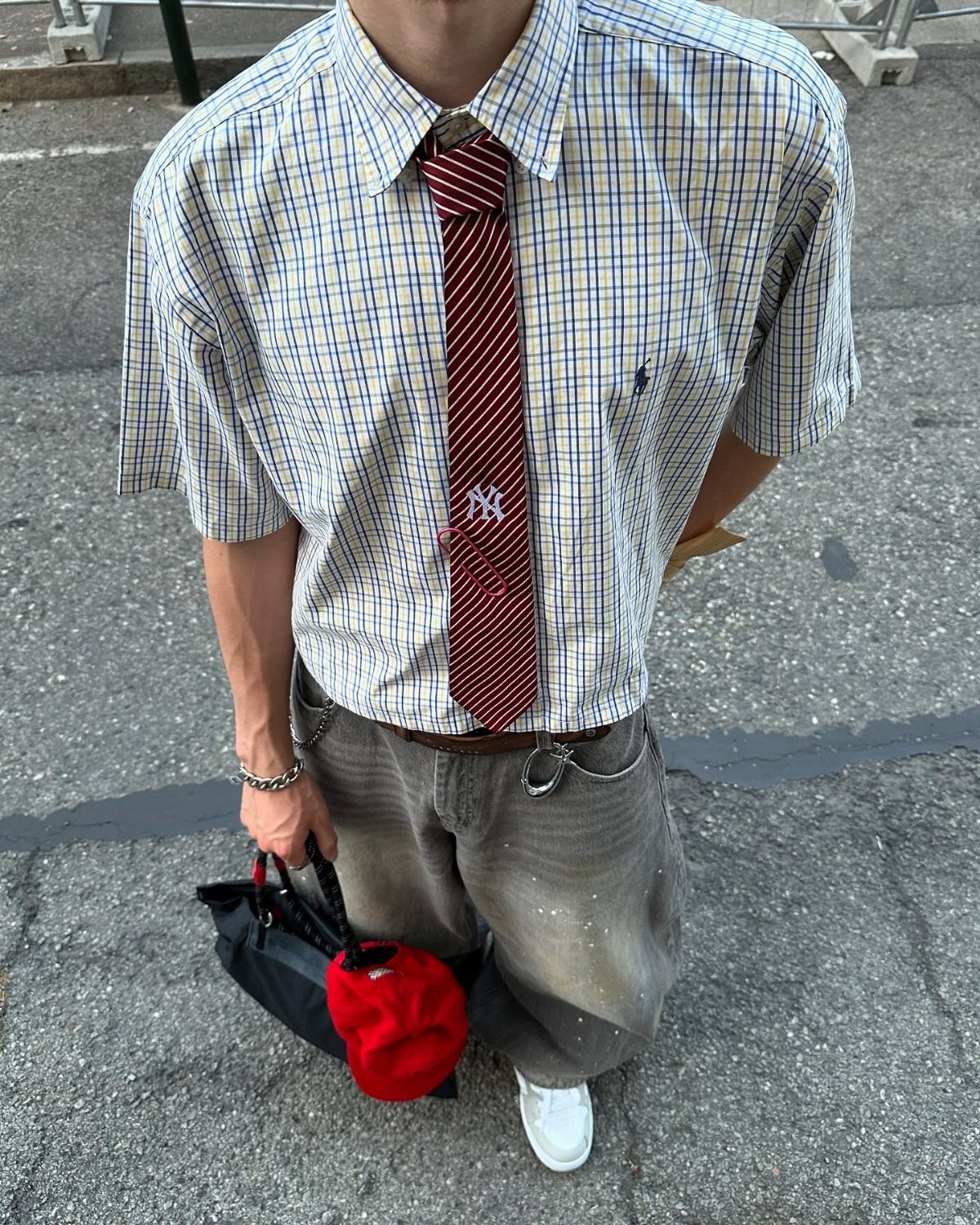 Person wearing a checkered short-sleeved shirt, a striped tie, and baggy grey trousers.