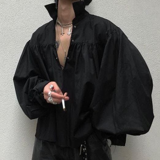 A person wearing a voluminous, oversized black flowy shirt with dramatic puffed sleeves and silver jewelry.