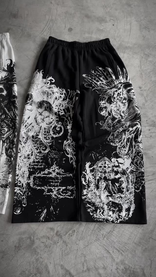 Black shorts with white gothic graphic prints lying on a grey concrete background.