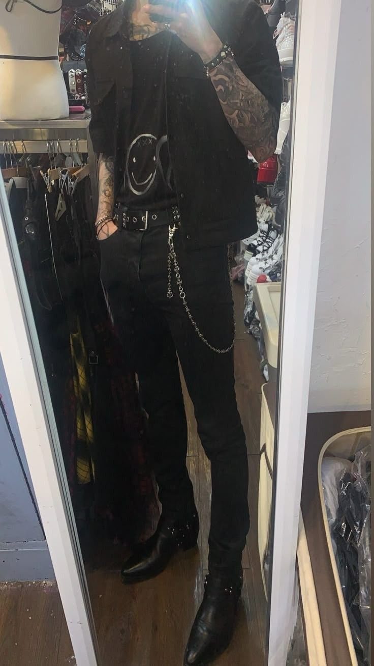 A person wearing an all-black outfit including slim-fit black jeans and a silver chain.