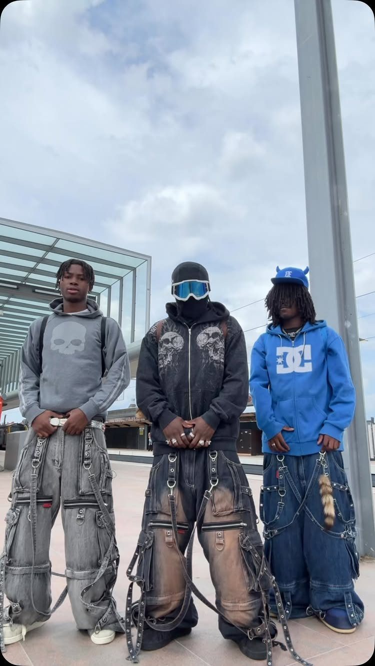 Three young men posing in oversized hoodies and heavily decorated, baggy cargo pants with chains.