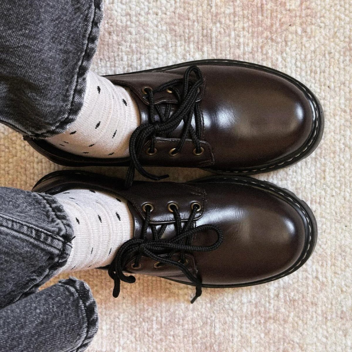 Dark brown leather oxford shoes with black laces worn with patterned socks and grey jeans.