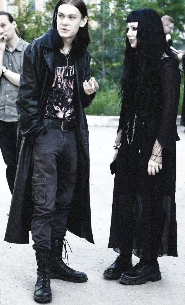 Two people dressed in black gothic attire standing together in an outdoor setting.