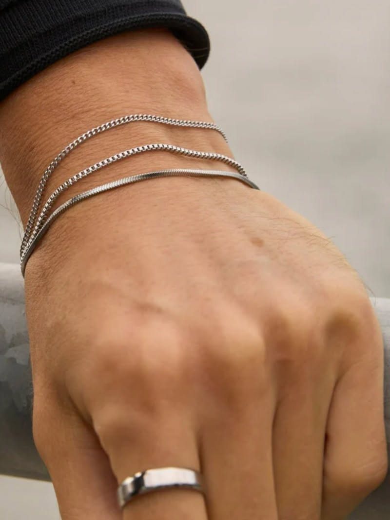A person's wrist wearing three thin silver bracelets and a simple silver ring.