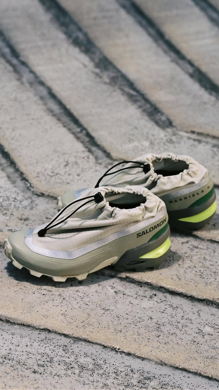 Salomon and Maison Margiela collaboration sneakers resting on a grey concrete ground.