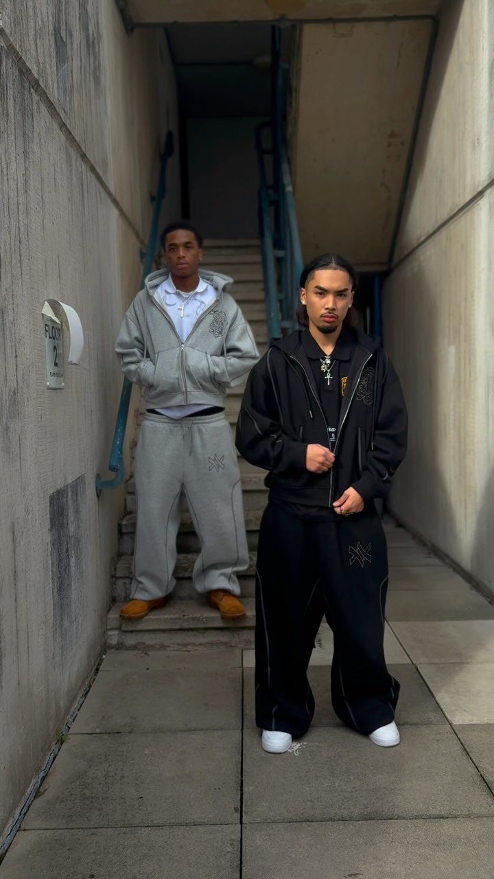 Two men posing in an urban concrete stairwell wearing stylish grey and black hoodies.