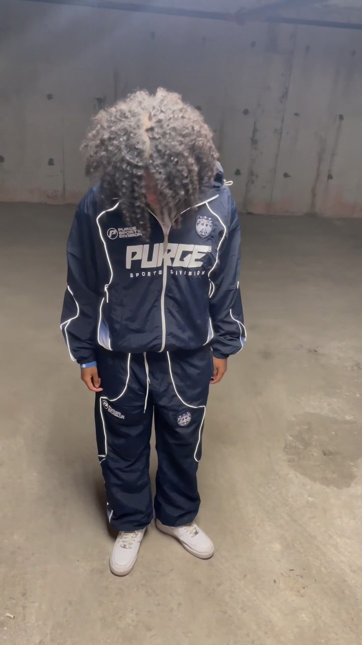 A person with voluminous curly hair wearing a navy blue tracksuit with white accents.