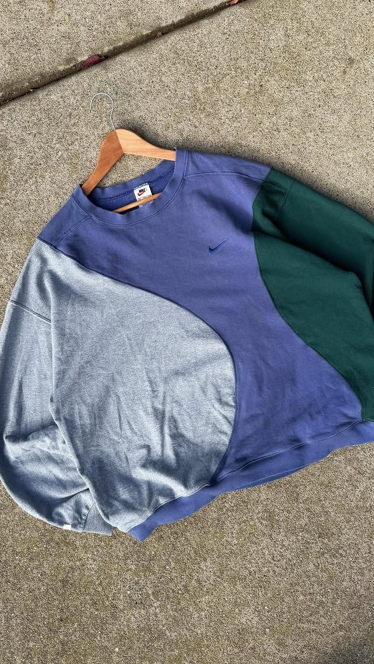 A multi-colored patchwork sweatshirt in blue, grey, and green lying on a concrete surface.