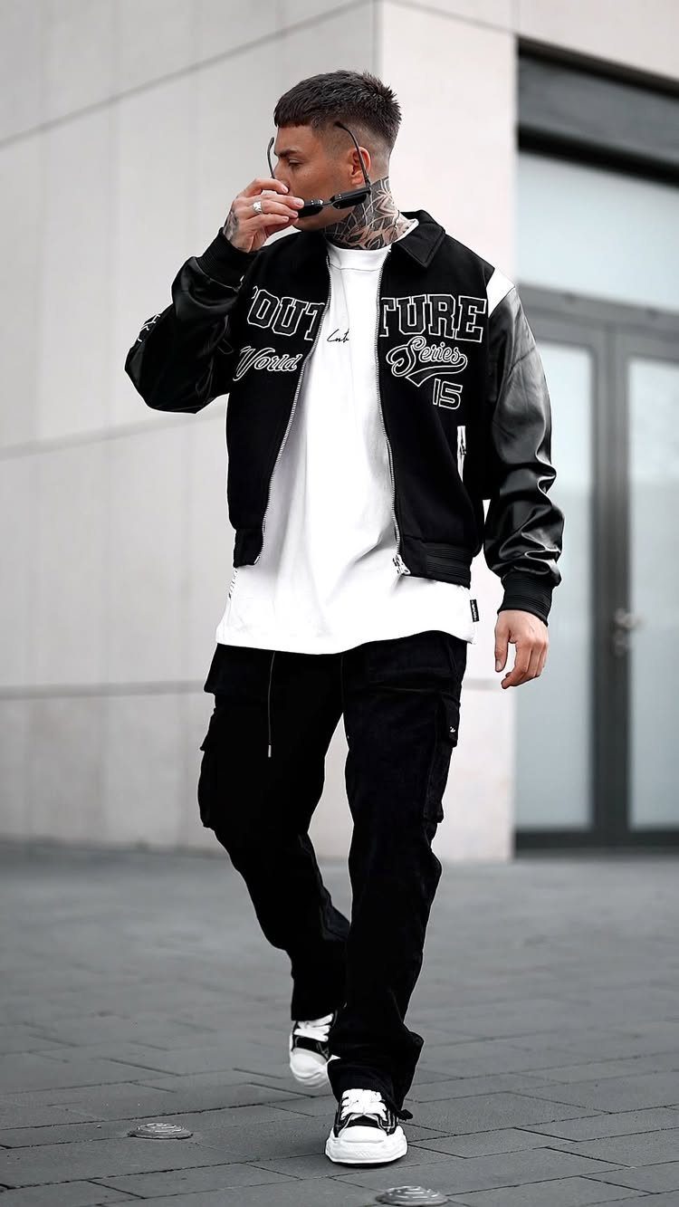 A man walking in a black and white varsity jacket, white t-shirt, and black cargo pants.