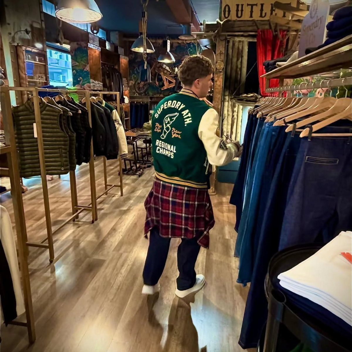 Man wearing a green varsity jacket browsing through blue jeans in a clothing store.