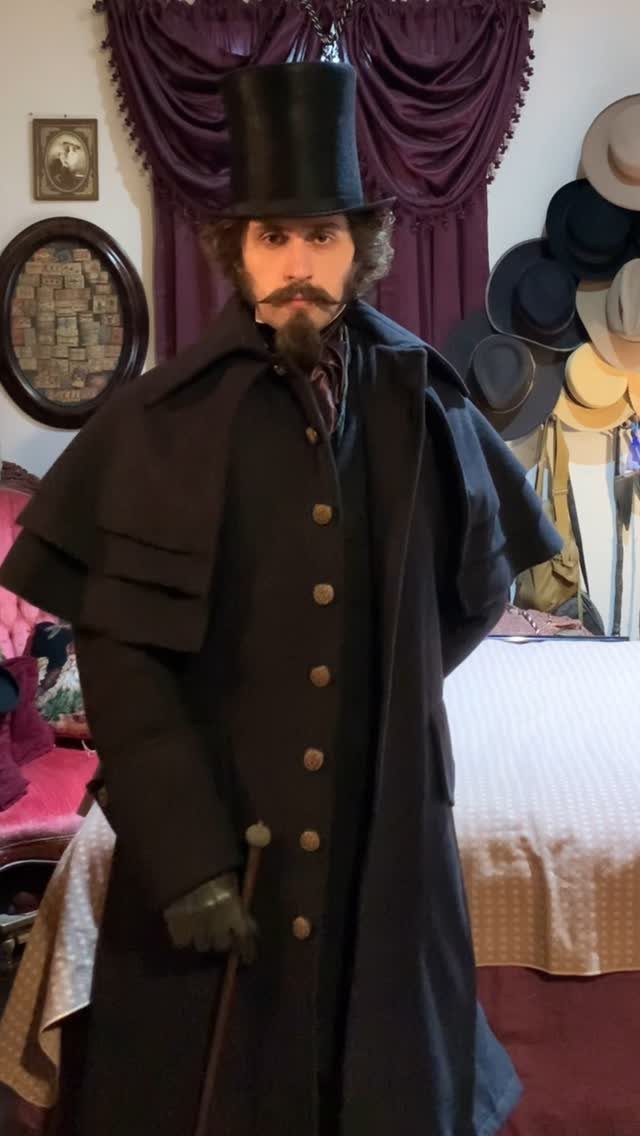 Man in Victorian goth attire featuring a top hat, long black cape coat, and cane.