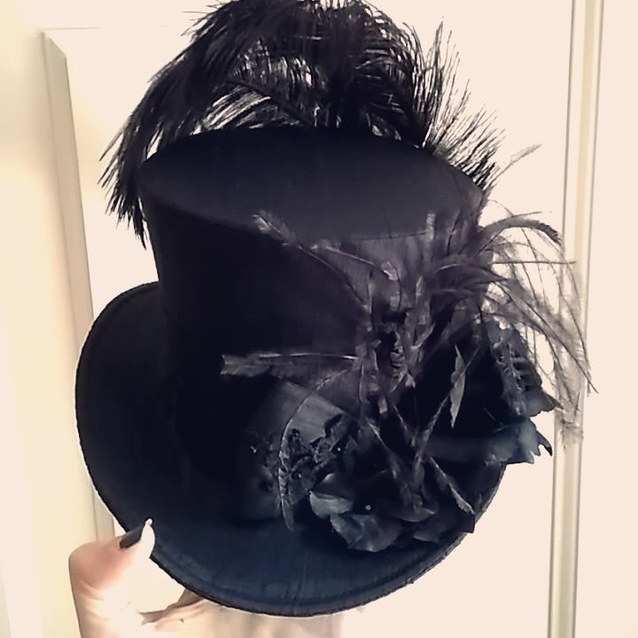 A black silk top hat adorned with large, dramatic black feathers held by a hand.