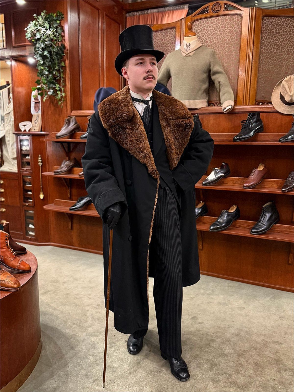 Man in Victorian gothic attire wearing a top hat, fur-collared coat, and holding a cane.