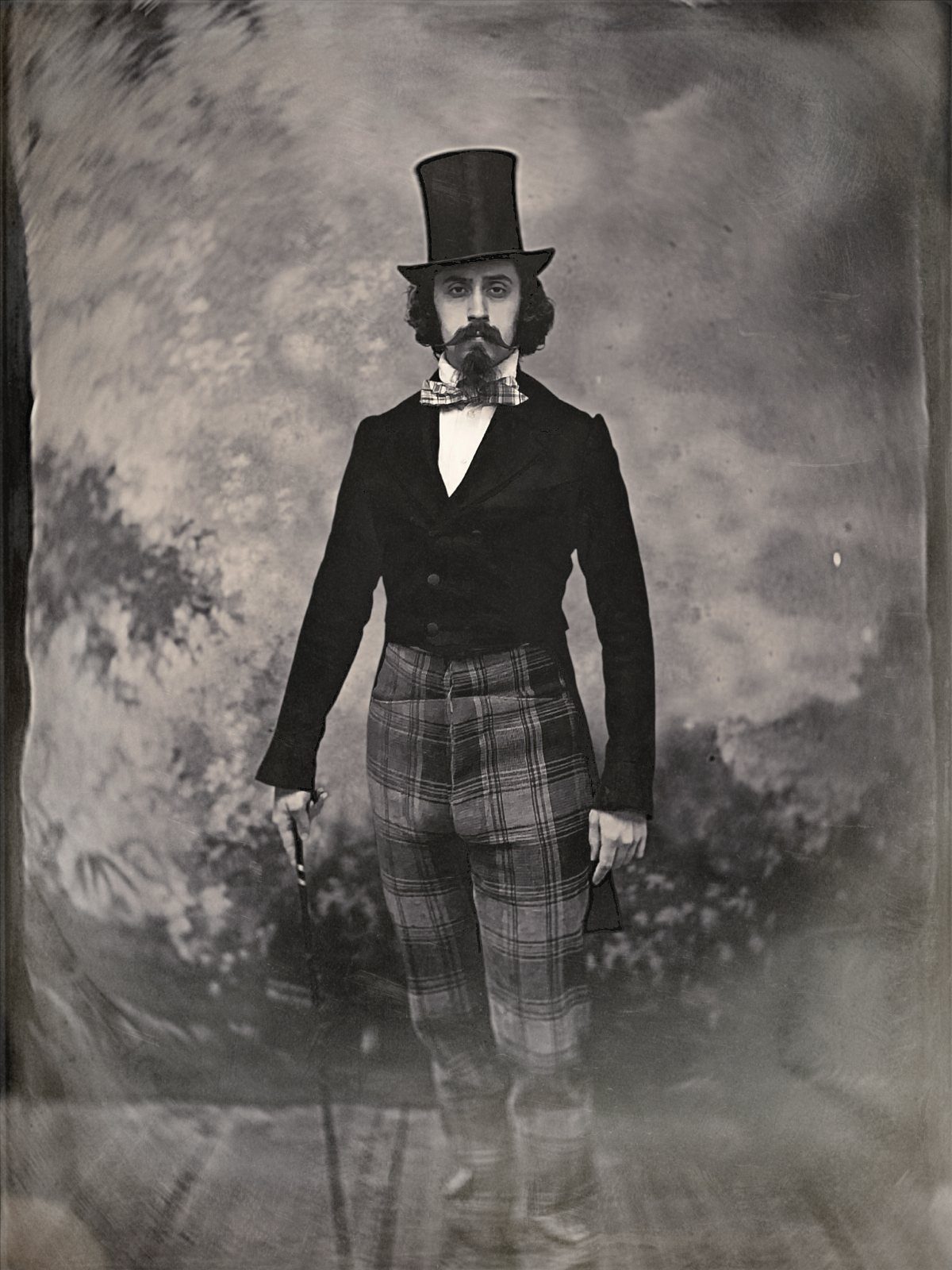 Man in Victorian top hat, dark jacket, and plaid trousers holding a cane.