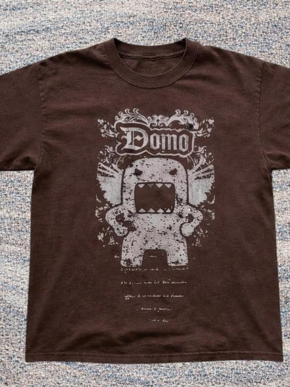 A brown t-shirt with a large white Domo character graphic printed on the front.