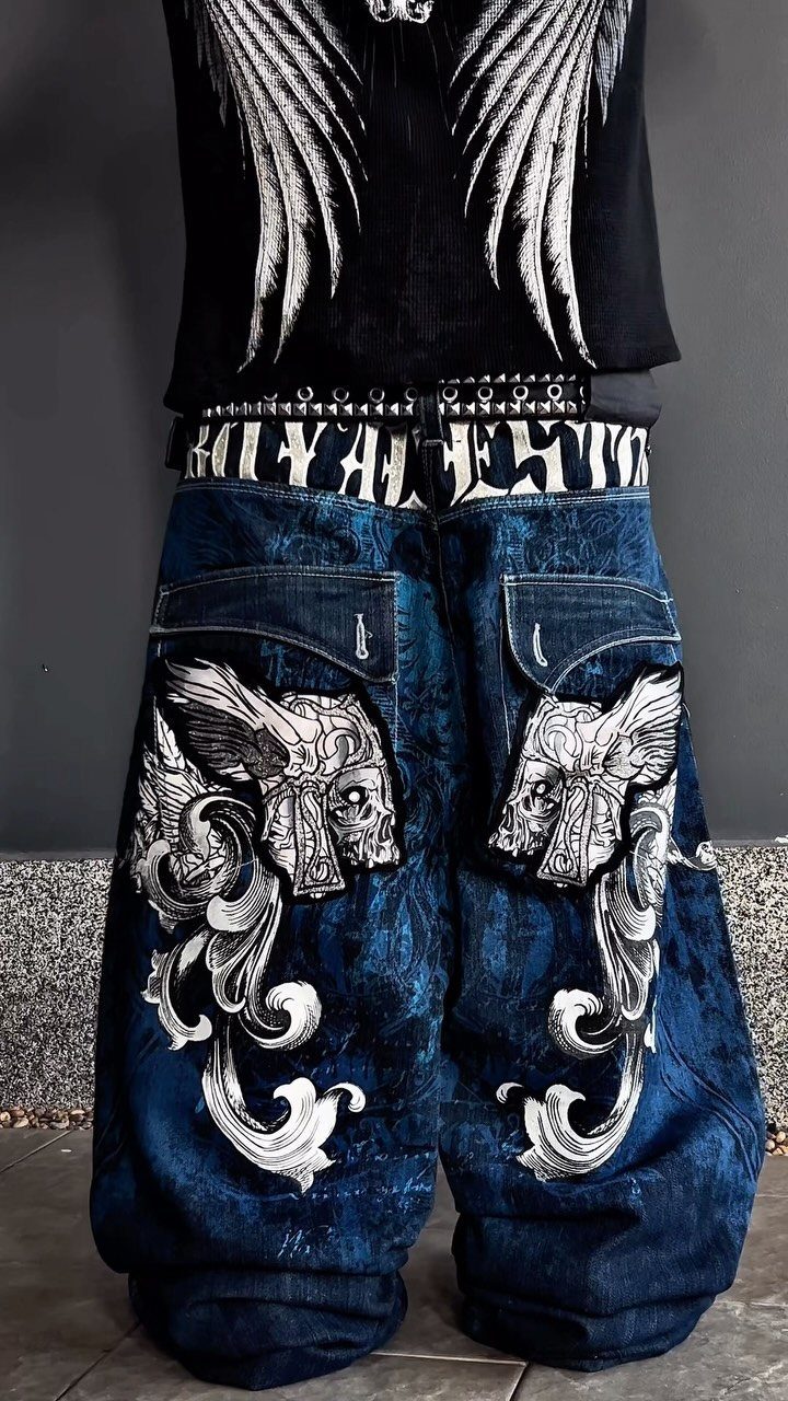 Person wearing oversized blue denim jeans with large white skull and wing graphics.