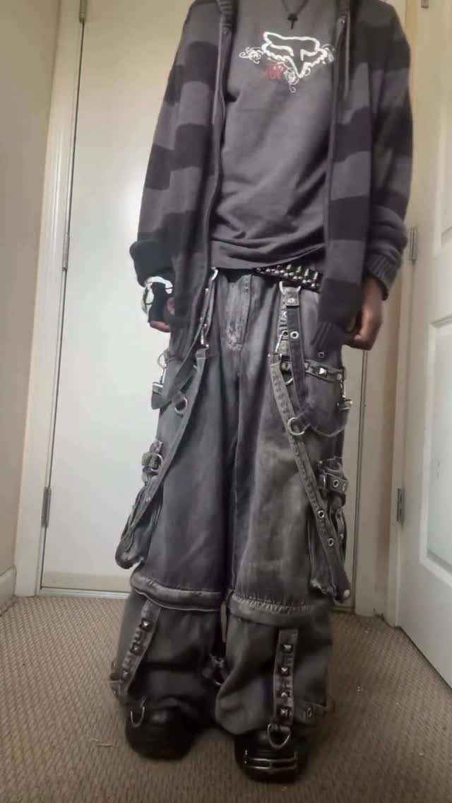 Person wearing oversized dark grey baggy cargo pants with metal rings and straps.