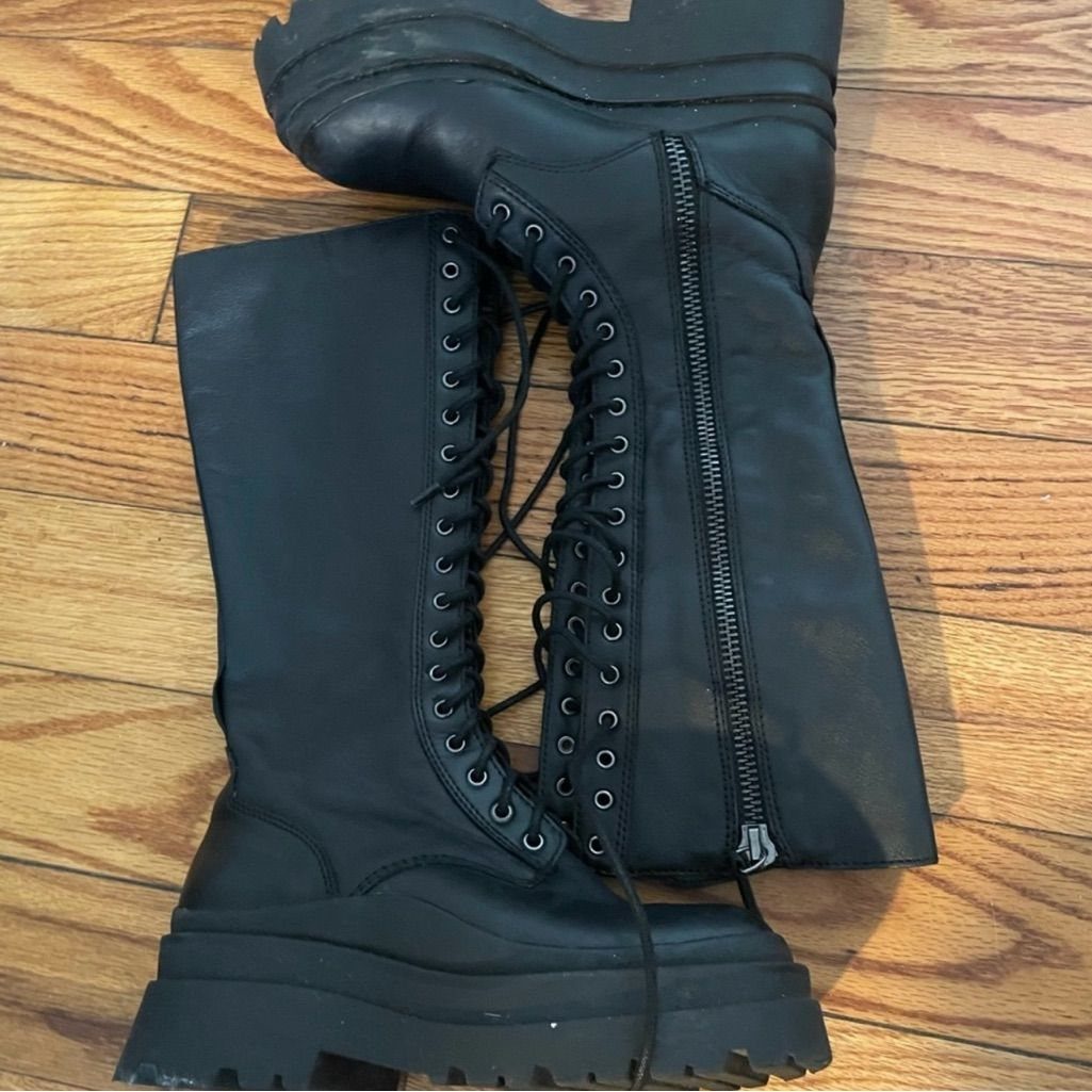 Black lace-up platform combat boots with side zippers resting on a wooden floor.