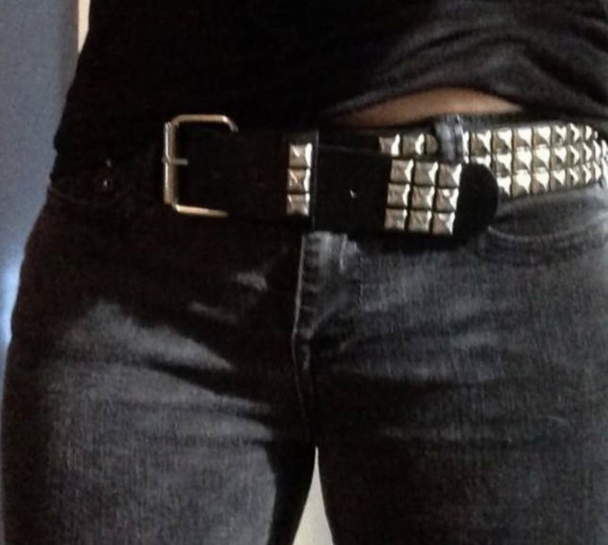 A wide black leather belt with large silver metal studs worn on dark denim jeans.