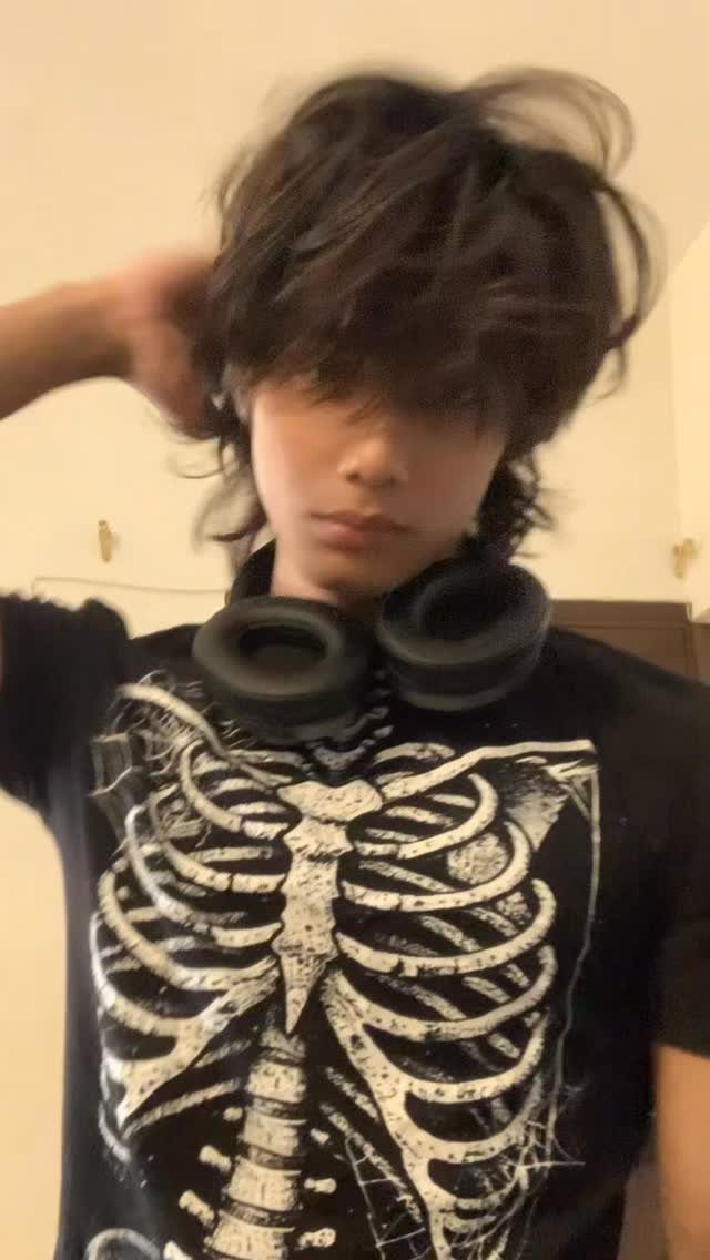 Person with dark hair wearing a black skeleton graphic t-shirt and headphones.