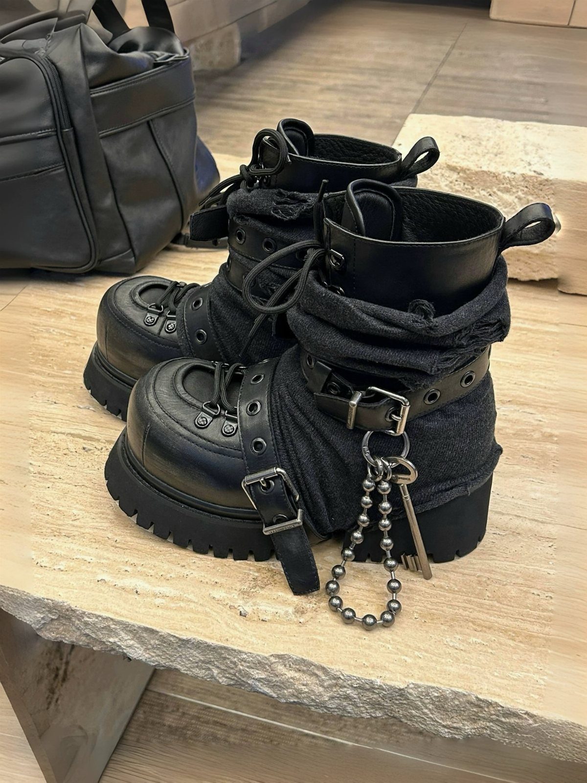 Black leather platform combat boots with silver buckles and a ball chain accessory on stone.