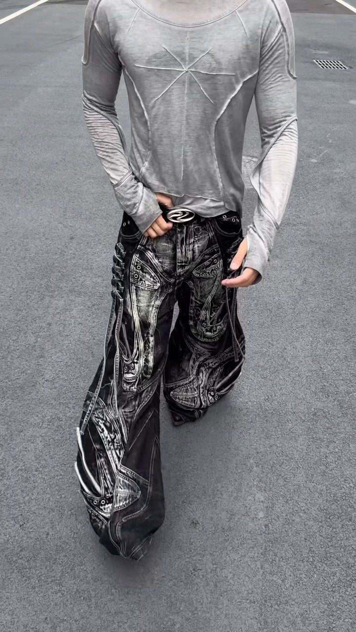 Person wearing baggy black denim jeans featuring large white skull graphic prints on asphalt.