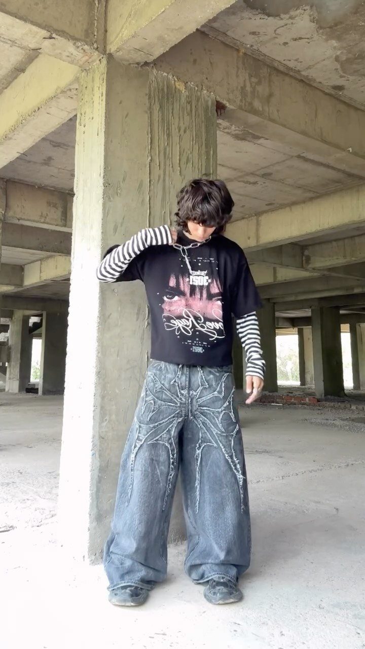 Person wearing a graphic t-shirt, striped long sleeves, and oversized patterned wide-leg denim pants.