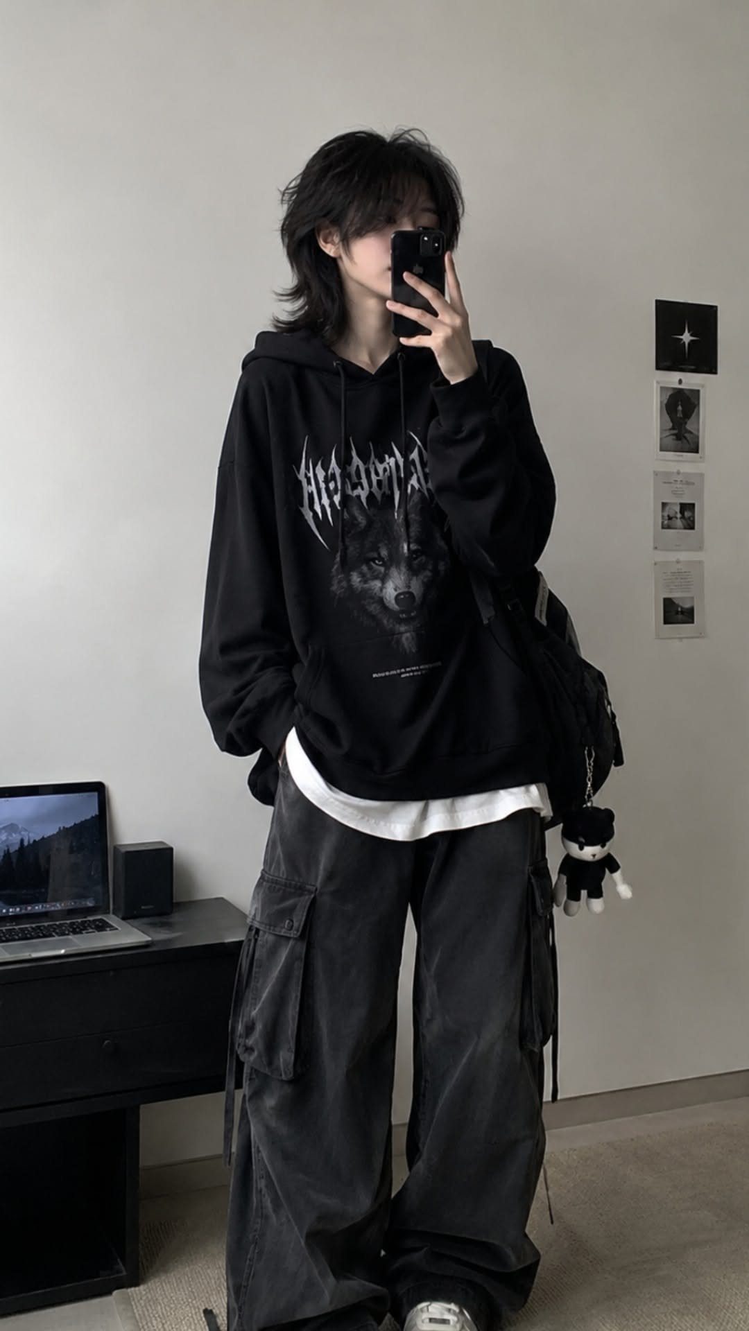 Person in a black oversized graphic hoodie and baggy cargo pants taking a mirror selfie.