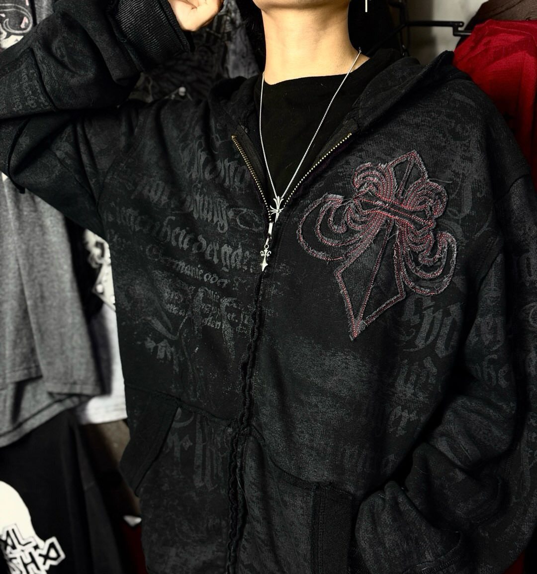 Person wearing a black oversized graphic zip-up hoodie with a large cross emblem.