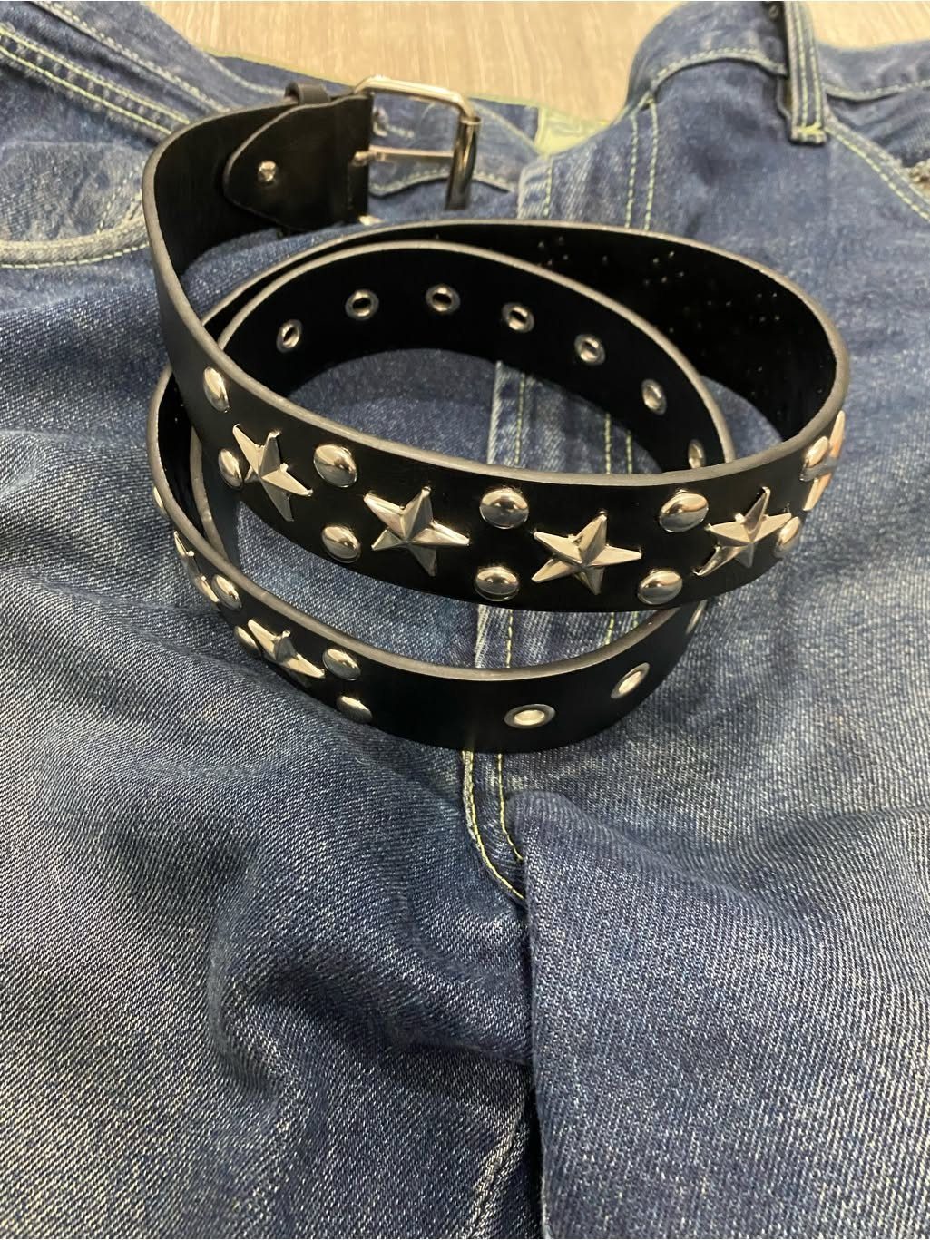 Black leather belt with silver star and circle studs resting on blue denim jeans.