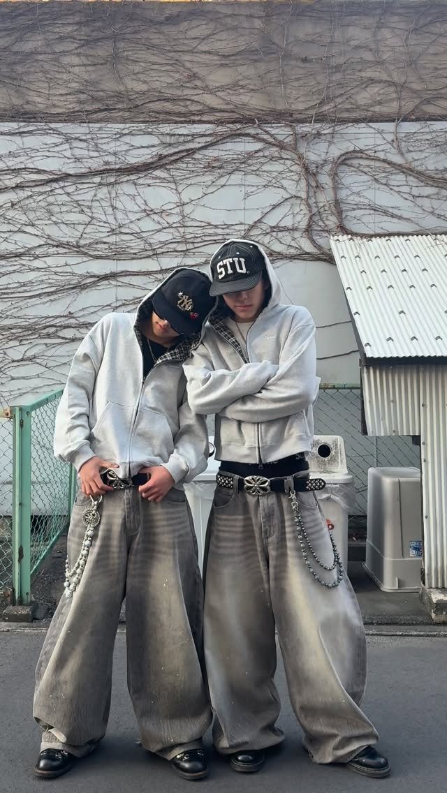 Two people wearing matching grey oversized hoodies and baggy grey trousers with silver chains.
